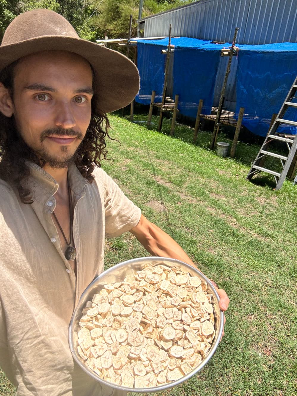 A person in a wide-brimmed hat holding a large bowl of pale dried green banana slices