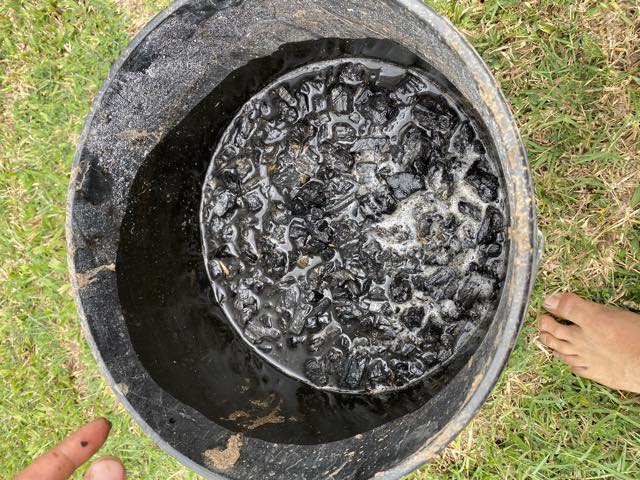 Charcoal soaking in liquid inside a drum, a bare foot beside it