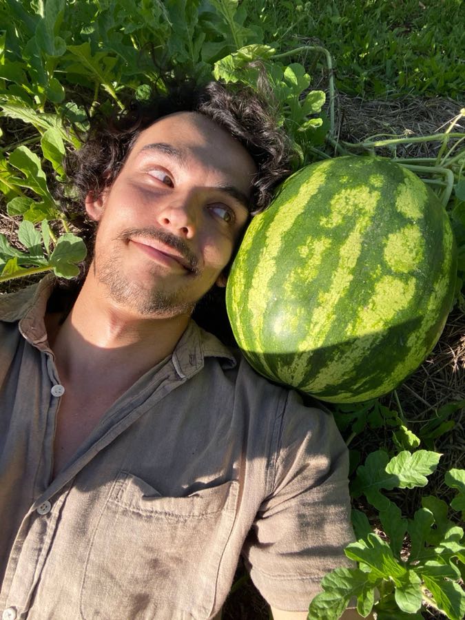 Joel lying in the watermelon patch beside a ripe watermelon