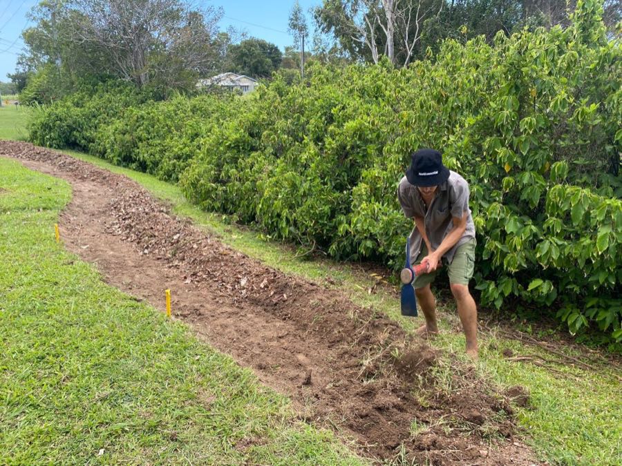 Joel digging a contour swale with a mattock beside a hedgerow