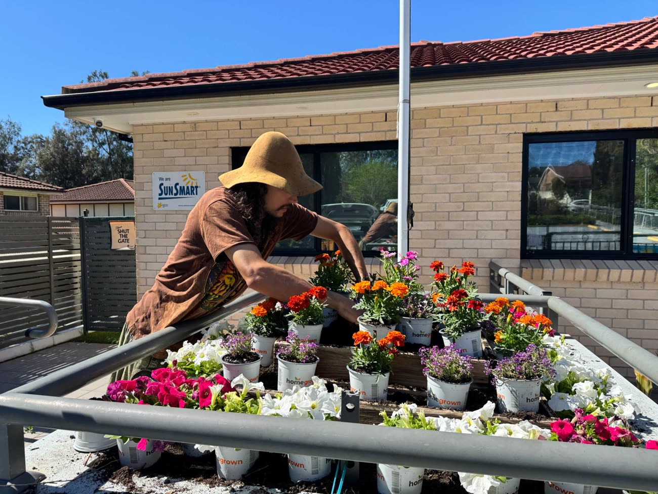 A person in a wide-brimmed hat arranging potted flowers across a tiered raised garden bed