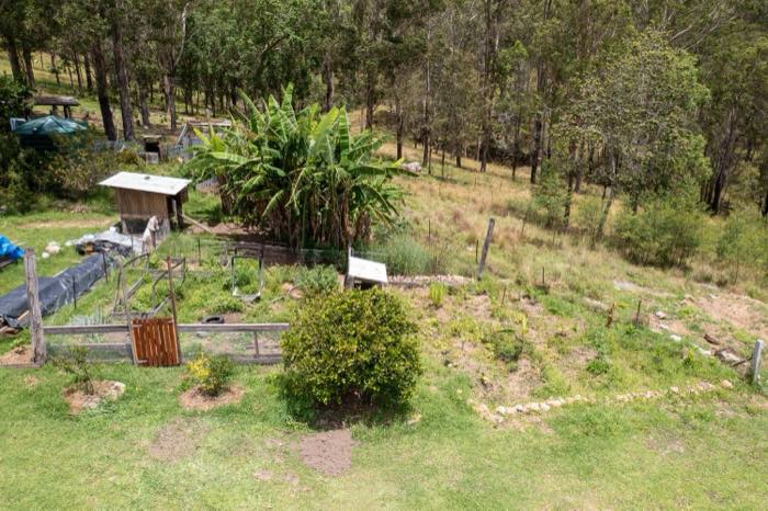 Elevated view of a fenced vegetable garden, chicken coop and large banana clump on a rocky slope