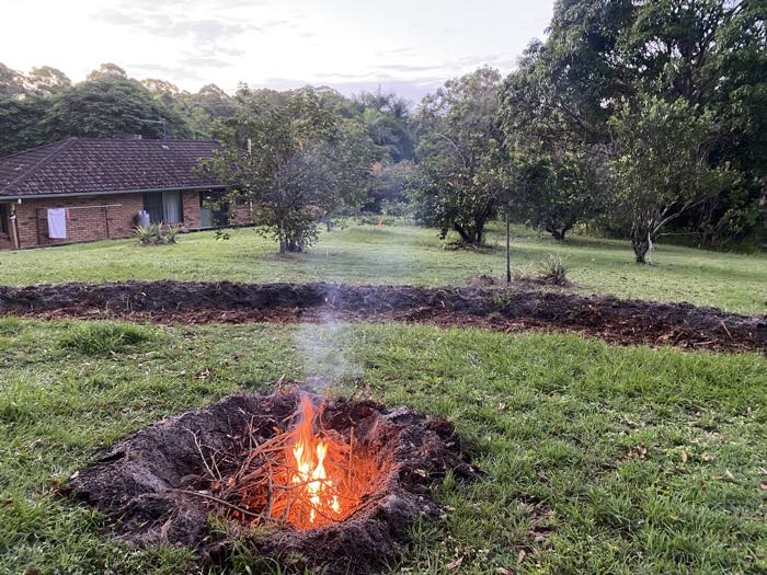 A small biochar burn in a pit on the grass, the new swale behind it