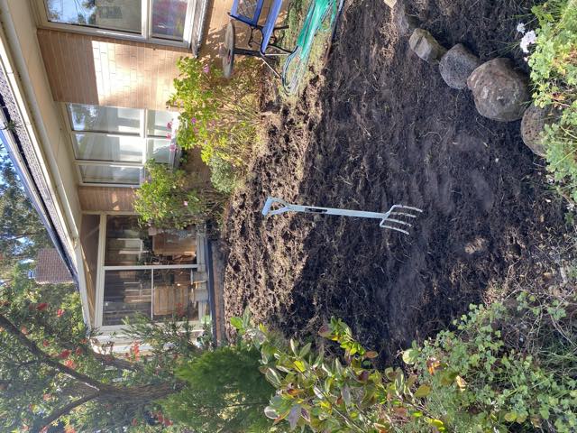 A freshly dug garden bed beside the house with a fork standing in it